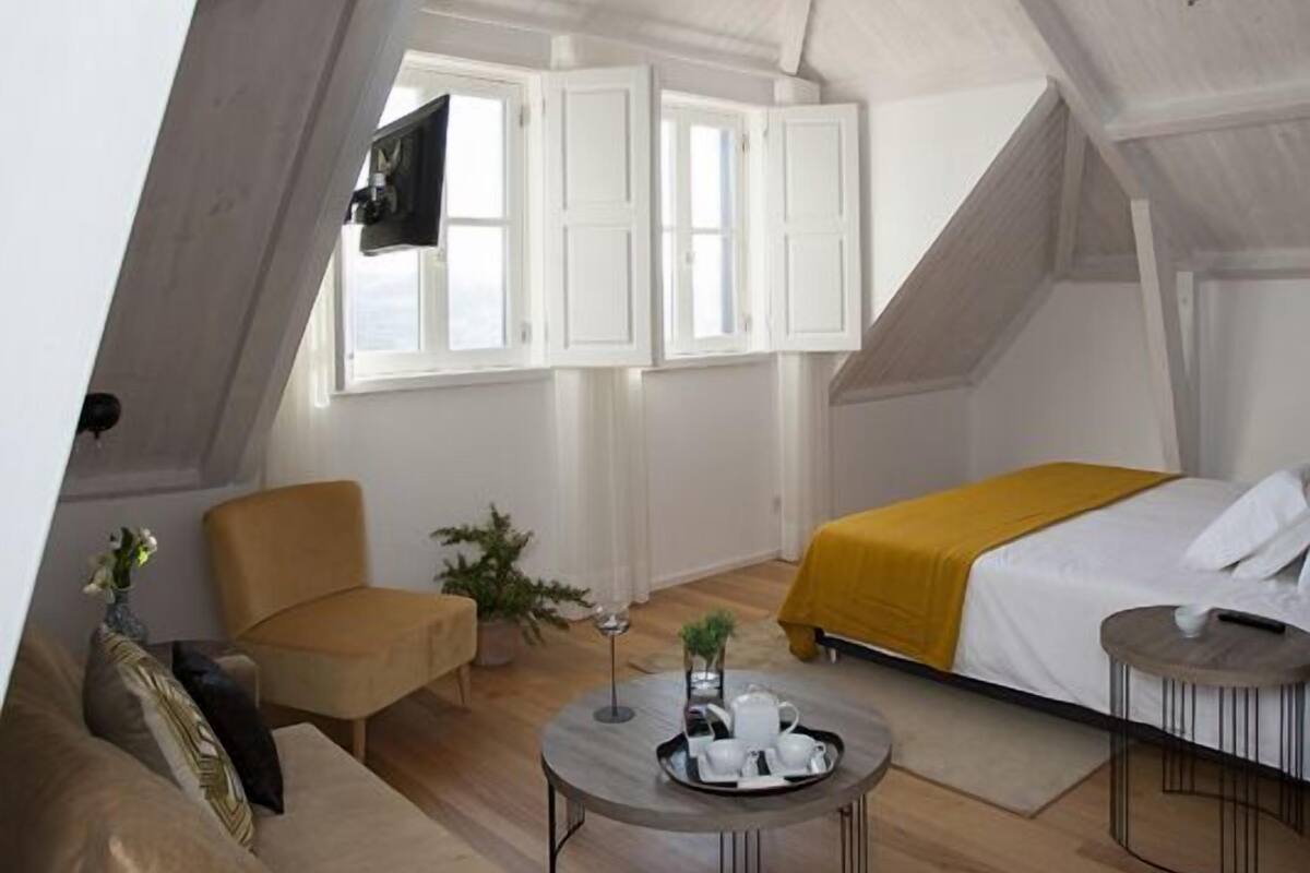 Un dormitorio tipo loft moderno con techo inclinado, un sofá, una cama y una mesita.