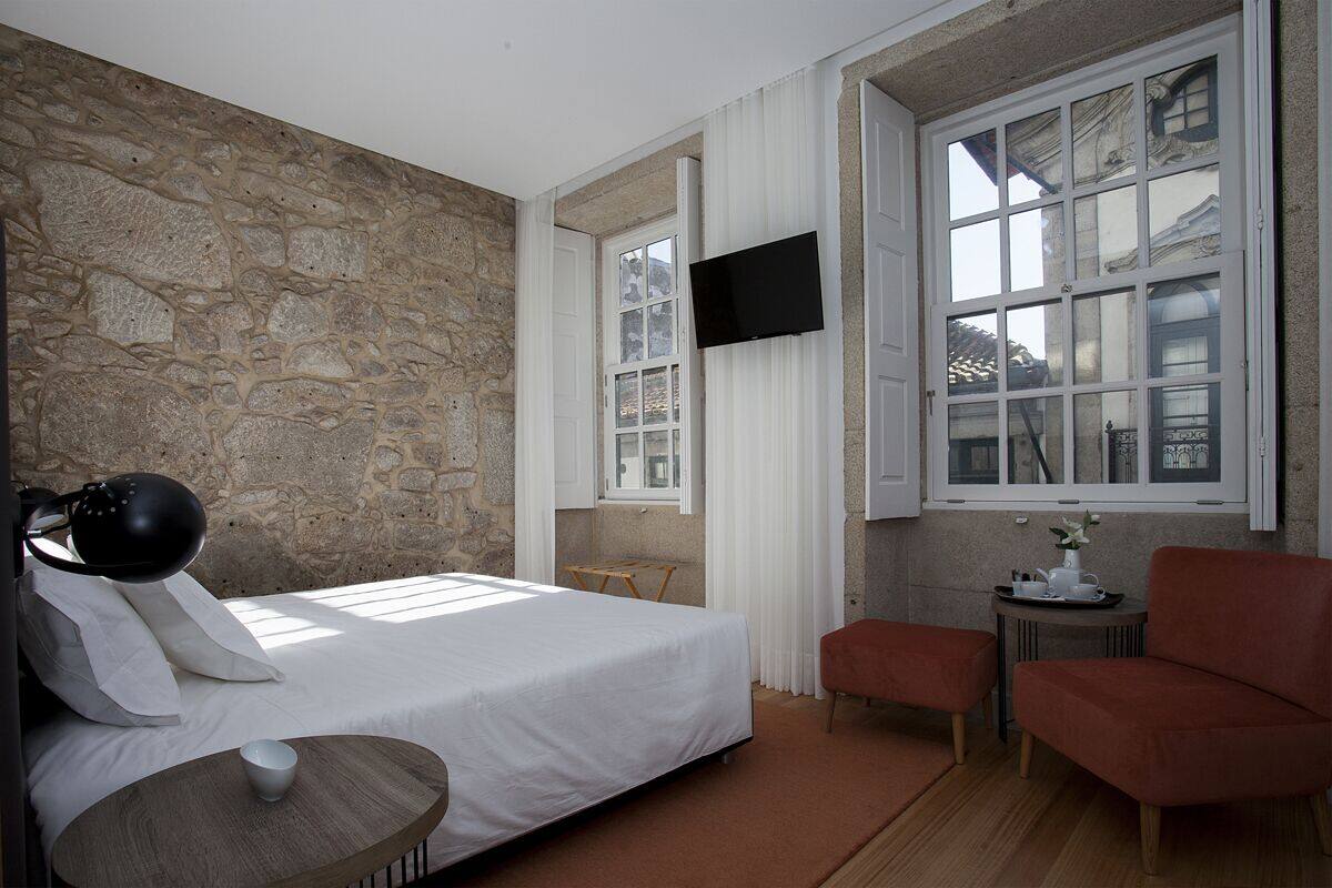 Un dormitorio con pared de piedra, cama, televisor, ventana y una mesita con una taza.