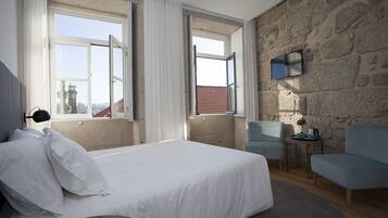 Un dormitorio con una cama grande, dos sillas, una mesita y una pared de piedra.