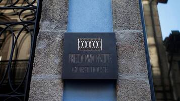 Placa da Guest House Belomonte, fixada numa parede de pedra com um portão de metal à esquerda.