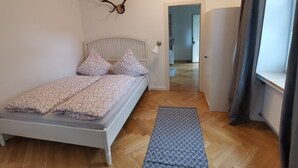 Ein Schlafzimmer mit einem Bett, floralem Bettbezug, einem Kopfteil, einem an der Wand befestigten Geweih und einem gemusterten Teppich. Eine Tür führt in einen anderen Raum.