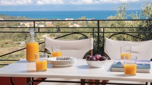 A table with breakfast items, a book, and a view of the sea.