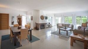 Un salon spacieux avec une cheminée, un coin repas avec des chaises en osier et un ensemble de canapés.