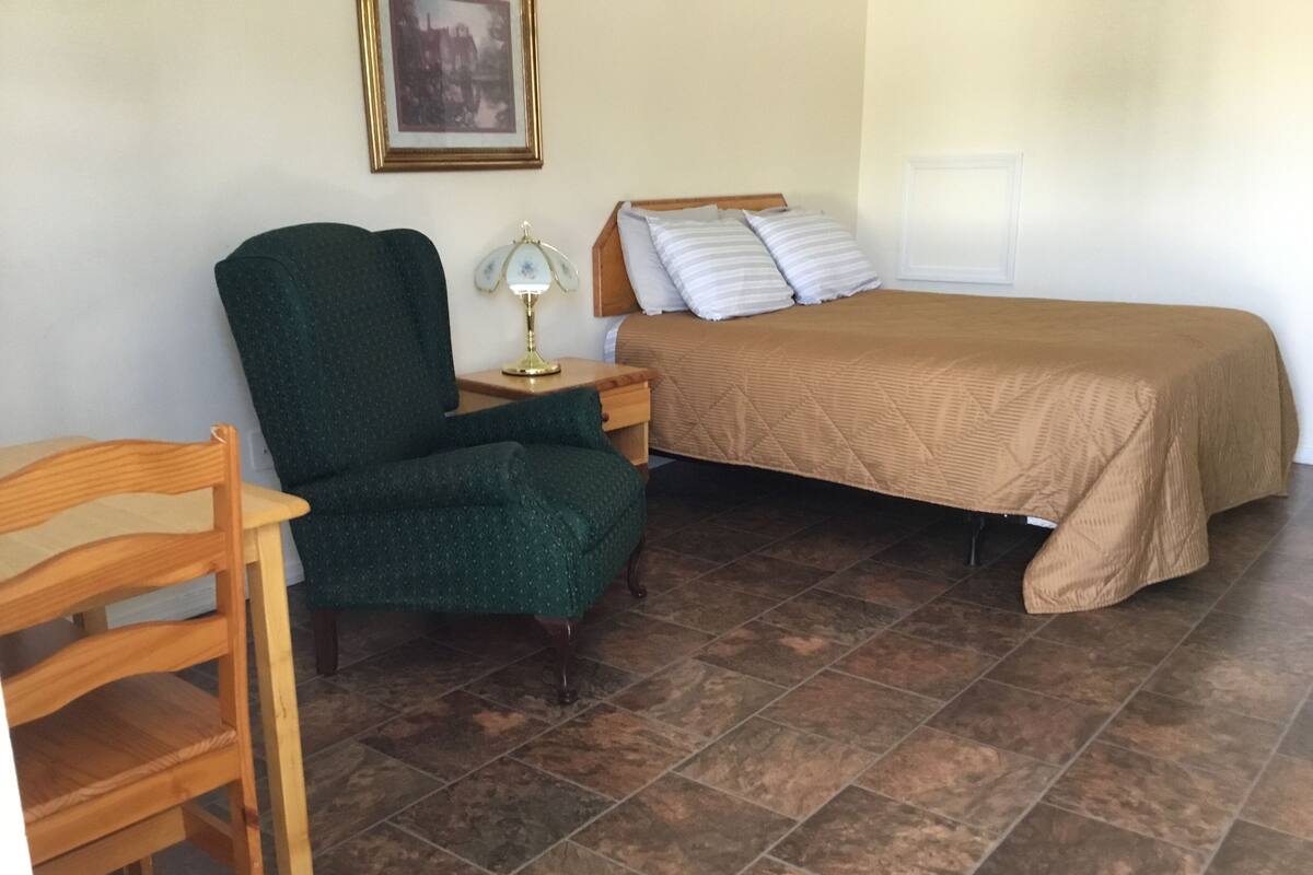 A bedroom with a bed, a chair, a nightstand, and a lamp.
