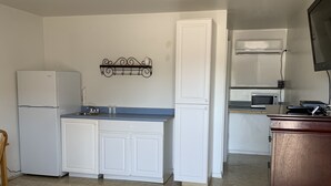 Cocina compacta con armarios blancos, un refrigerador, un microondas y una estufa. Hay un pequeño comedor con una silla y una mesa.