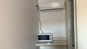 Un pasillo estrecho con una pared blanca, un microondas en un estante y una puerta al final.