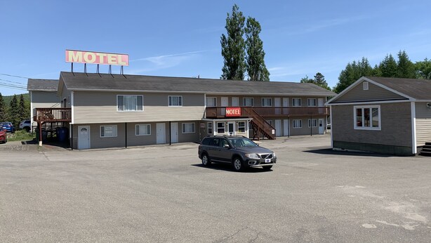 Un motel con un edificio de dos pisos, una zona de estacionamiento techada y una estructura pequeña contigua.