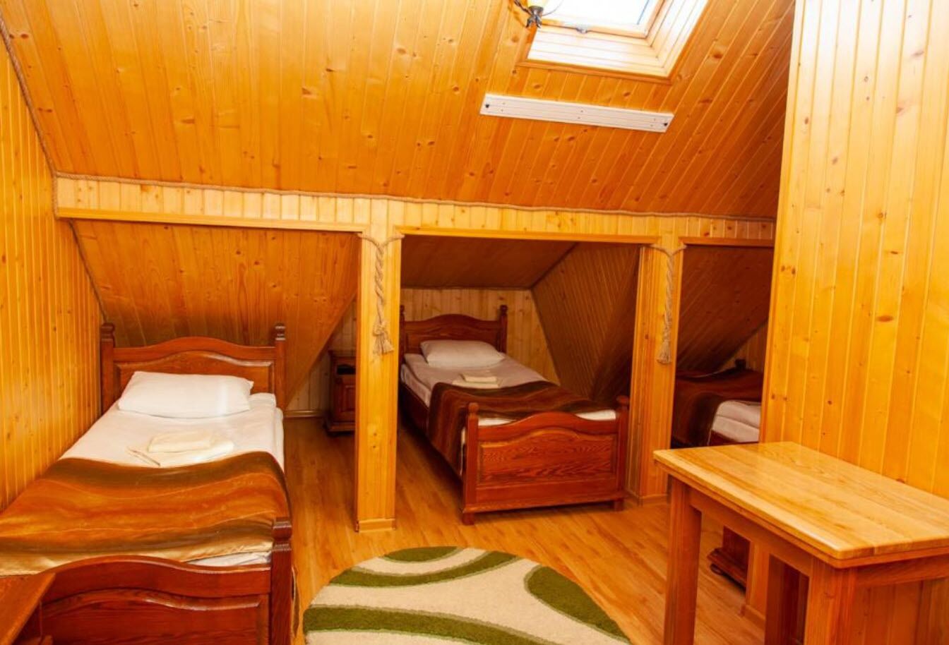 A wooden cabin with three wooden beds, a skylight, and a small wooden table.