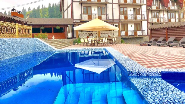 A hotel with a swimming pool, outdoor seating, and a mountain backdrop. - Villa Nikoletta (Bukovel)