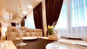 A dining area with a table set for two, featuring a dark patterned tablecloth, a tufted headrest, and a vase with yellow flowers. - Villa Nikoletta (Bukovel)