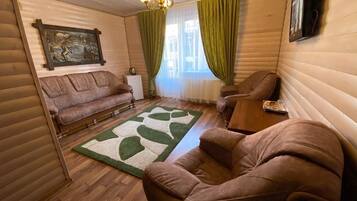 A cozy room with a wooden floor, a green and white rug, a brown sofa, a brown armchair, and a small table.