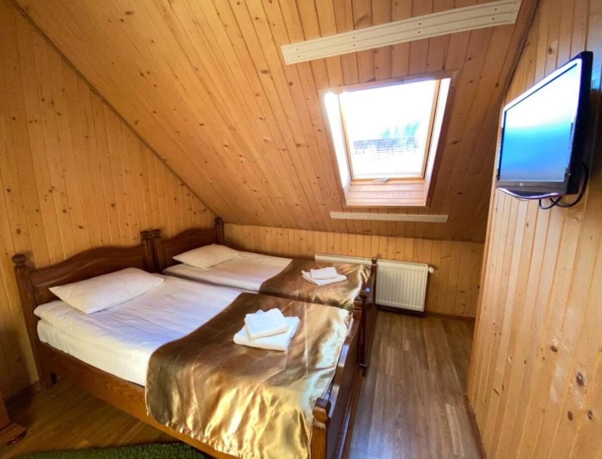Una habitación tipo cabaña de madera con dos camas, un televisor y un tragaluz.