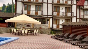 A multi-story building with balconies, a pool area with lounge chairs, and a covered patio with tables and chairs. - Villa Nikoletta (Bukovel)