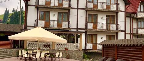 A multi-story building with balconies, a pool area with lounge chairs, and a covered patio with tables and chairs.
