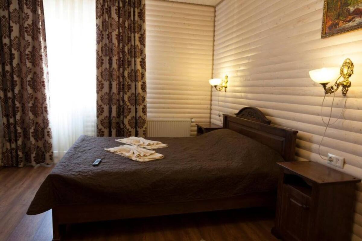 A hotel room with a large bed, two bedside lamps, a nightstand, and a window with curtains.
