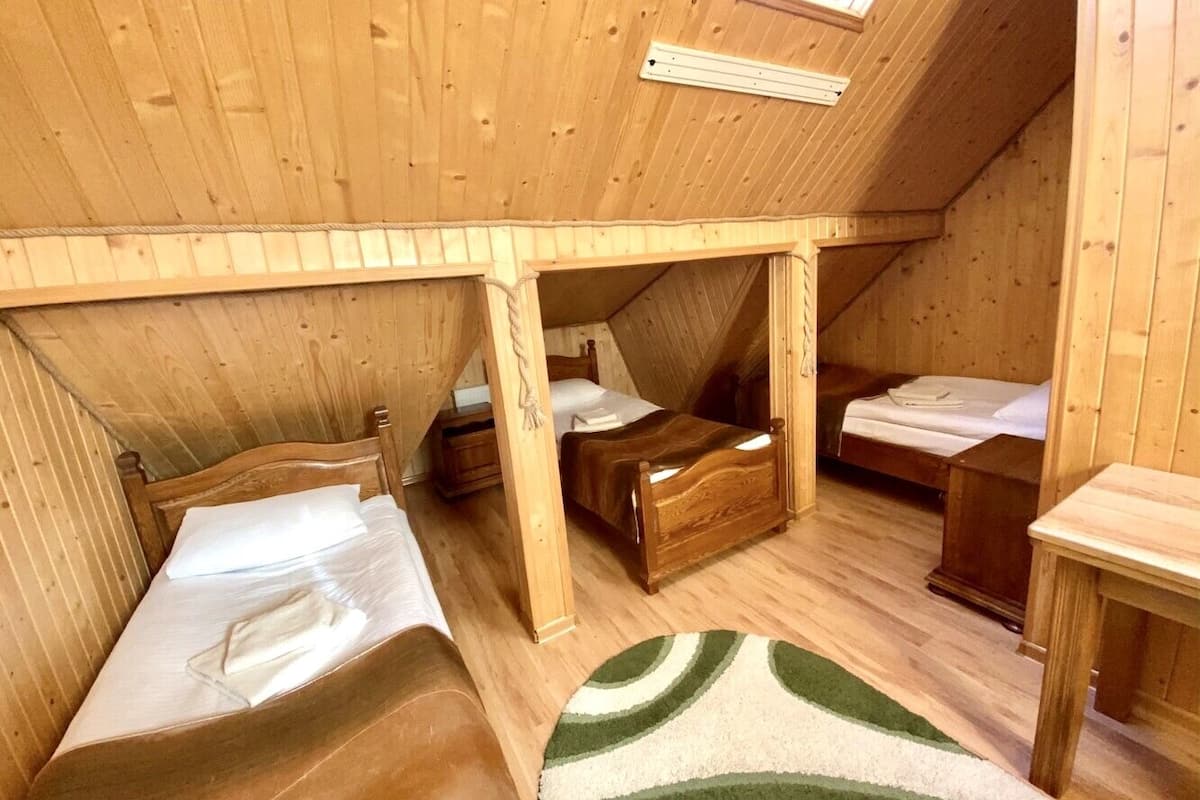 A small, wooden cabin with a sloped ceiling, three wooden beds, and a single table.