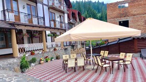 An outdoor patio with stone flooring, tables, chairs, and a large umbrella. - Villa Nikoletta (Bukovel)