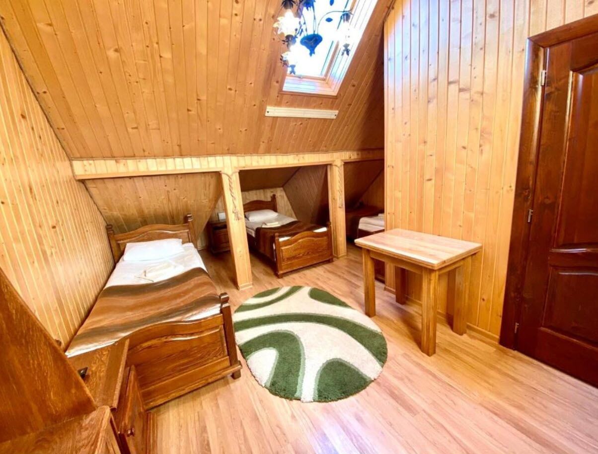 Een gezellig slaapkamer op zolder met houten wanden en een dakraam. Er staan twee houten bedden, een klein tafeltje en een groen-witte vloerkleed.