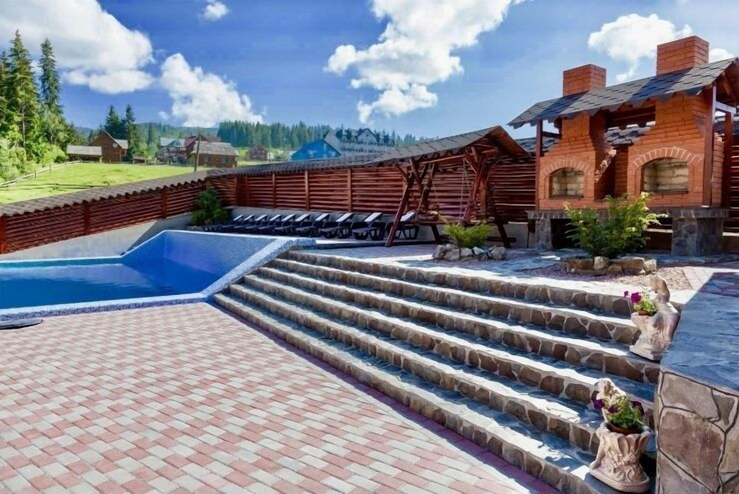 A pool area with steps leading to a wooden deck, surrounded by a wooden fence and a stone wall.