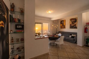 A living room with a dining area, a grey sofa, a table with a black tablecloth, and a bookshelf with various items. - House Cloe panoramic terrace sea view (Taormina)