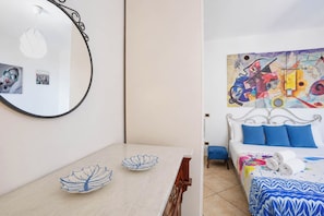 A room with a bed, a white headboard, and a colorful abstract painting on the wall. - House Cloe panoramic terrace sea view (Taormina)