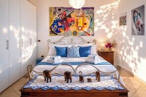 A bedroom with a bed, a nightstand, a lamp, a painting, and a wall-mounted picture. - House Cloe panoramic terrace sea view (Taormina)