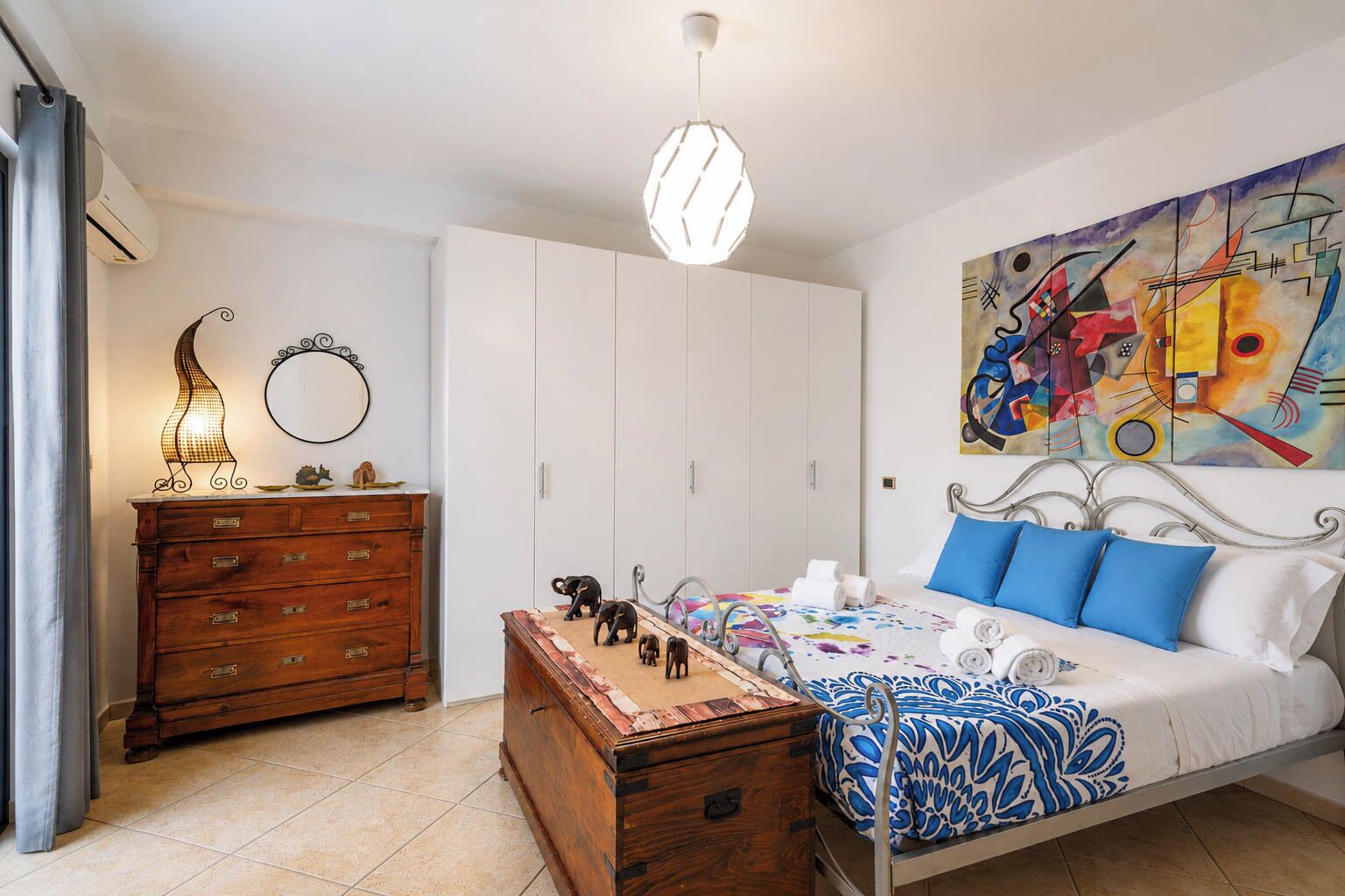 A bedroom with a bed, a dresser, a mirror, and a painting on the wall.