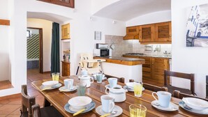 A dining area with a wooden table set for breakfast, a kitchen in the background, and a ceiling fan. - Wonderful private villa for 8 guests with private pool, TV and patio (Albufeira)