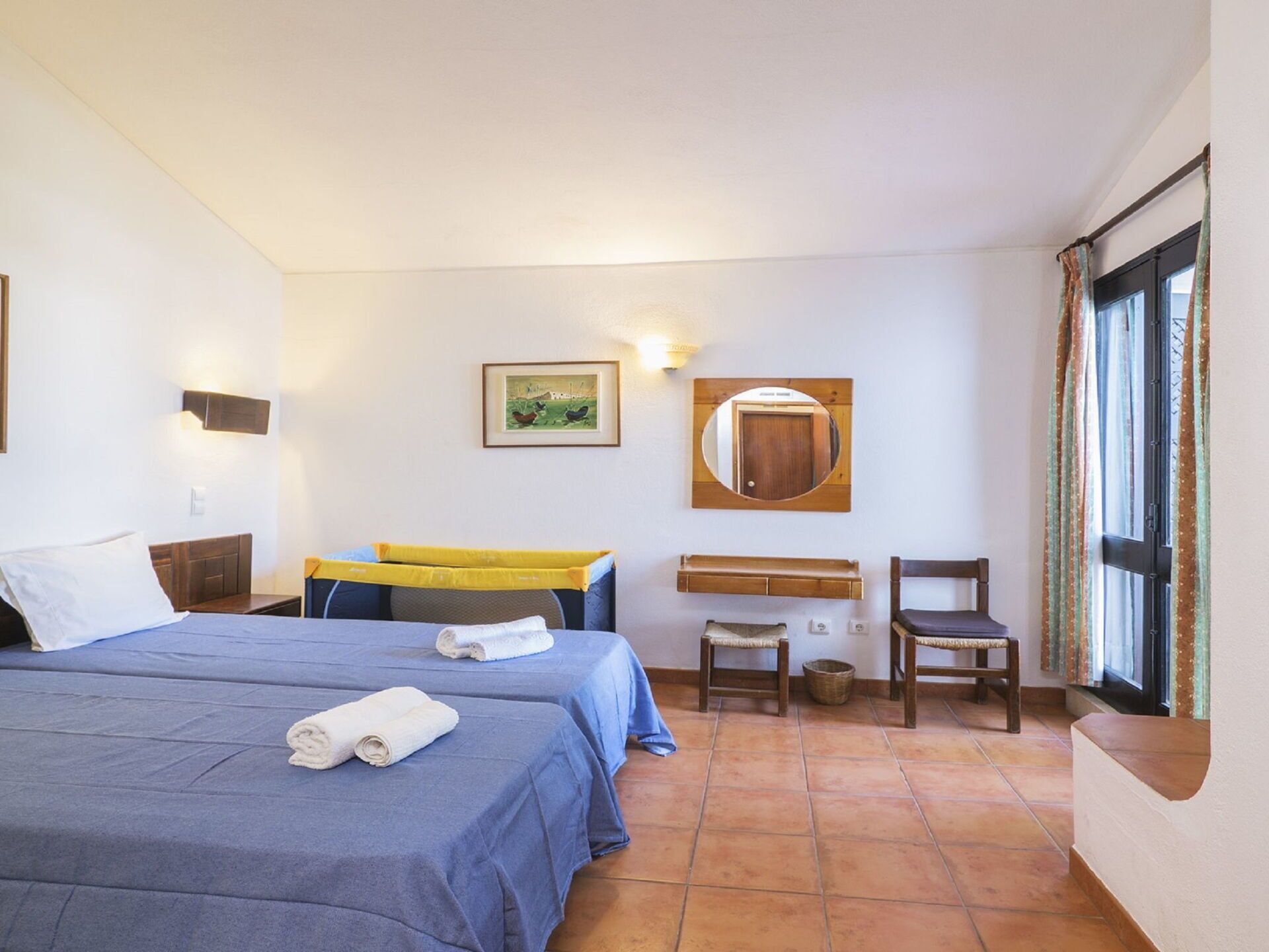 Habitación de hotel con dos camas, un escritorio pequeño, una silla, un espejo y una ventana con cortinas.