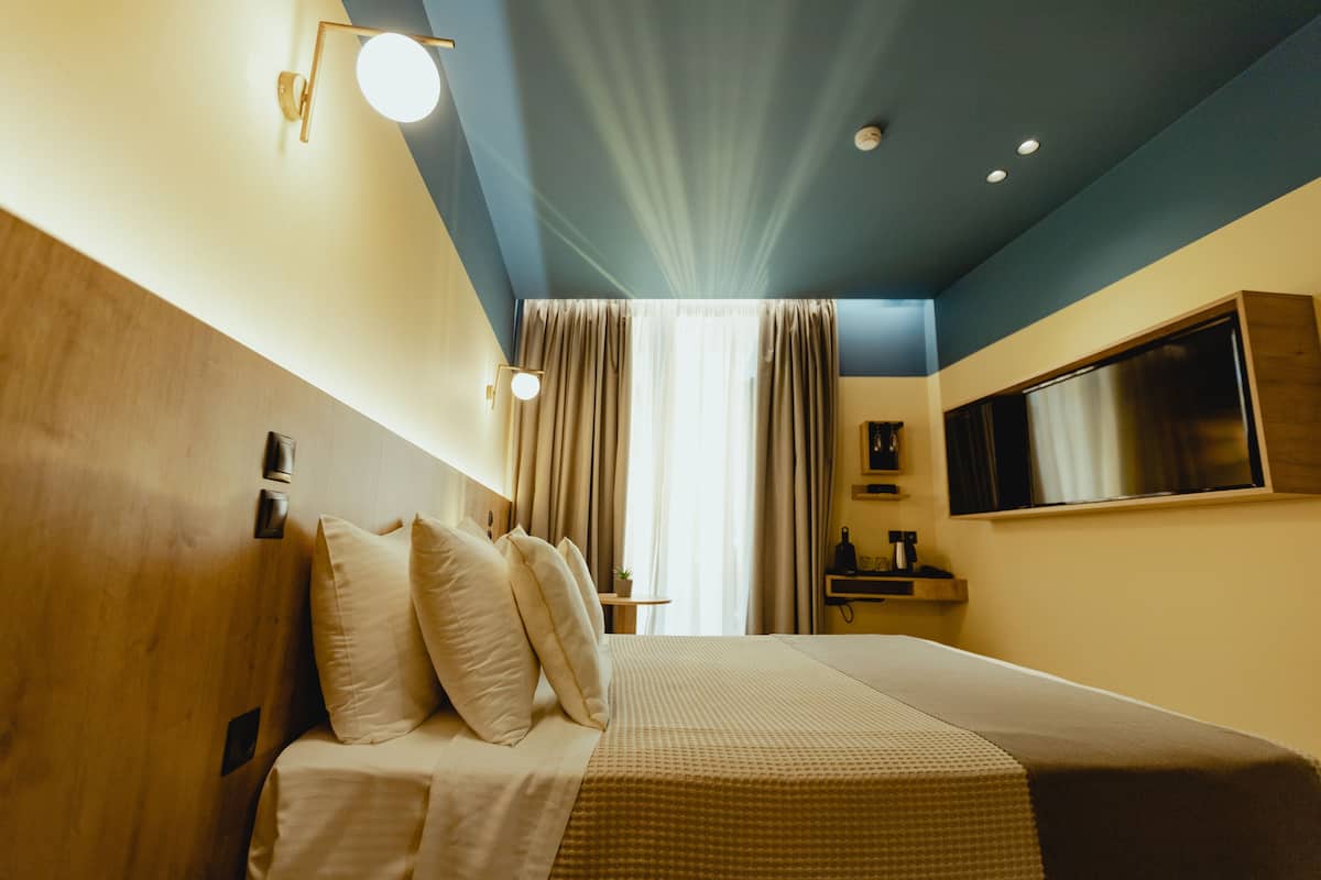 A hotel room with a bed, curtains, a TV, and a wooden headboard.