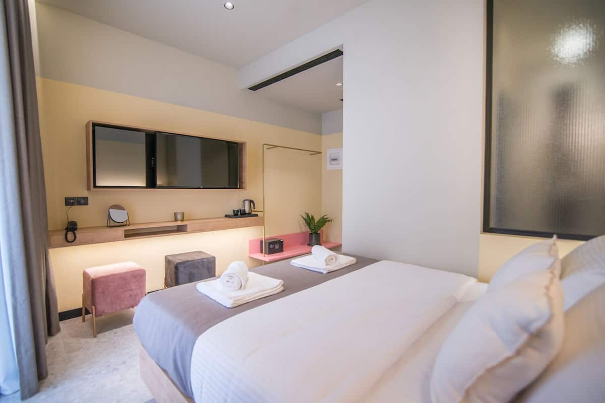 A modern hotel room with a large bed, a bedside table with a lamp, a small seating area, and a large mirror.