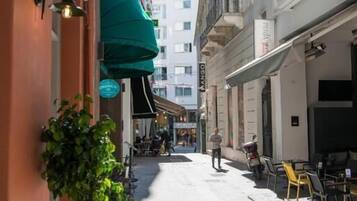 Eine enge Straße mit Außenplätzen, einem Schild für 'Athens Club' und einem Gebäude mit einem Balkon.