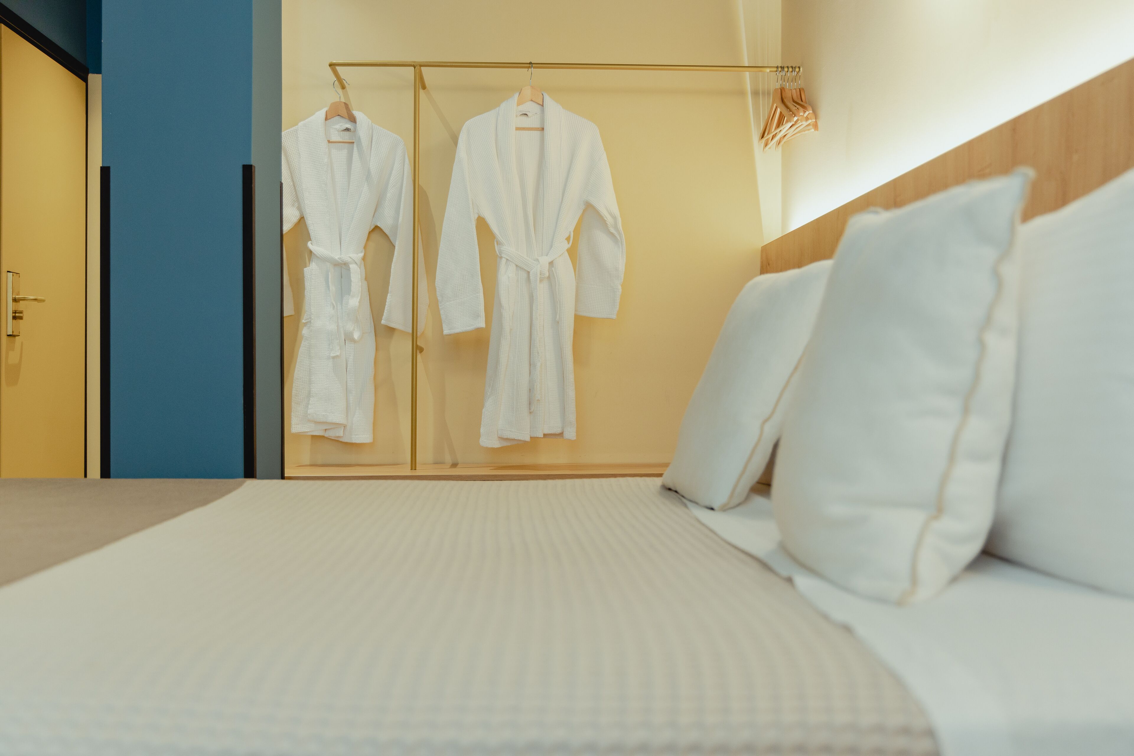 Una habitación de hotel con una cama, un armario con dos batas blancas y un cabecero de madera.