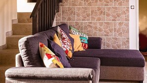 A living room with a stone wall, a dark wooden staircase, and a cushioned sectional sofa. - Beautifully Renovated, French Barn, Pet Friendly with WIFI (Saint-Plantaire)