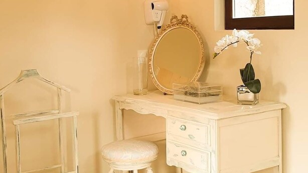 A white vanity with a round mirror, a stool, and a wall-mounted light fixture.