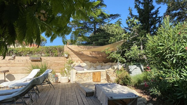 A wooden deck with lounge chairs, a stone bench, and a shaded seating area with cushions. - VILLA PROVENÇALE with private pool (between Aix and Marseille) (VELAUX)