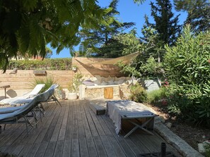 Um deck de madeira com espreguiçadeiras, um banco de pedra e uma área de estar coberta com almofadas.