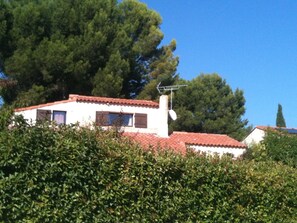 A white building with a red-tiled roof, surrounded by dense green foliage. - VILLA PROVENÇALE with private pool (between Aix and Marseille) (VELAUX)