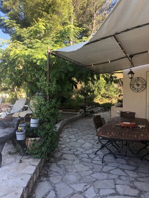An outdoor patio with stone flooring, a wooden table, and chairs. There are potted plants and a pergola with a canopy. - VILLA PROVENÇALE with private pool (between Aix and Marseille) (VELAUX)