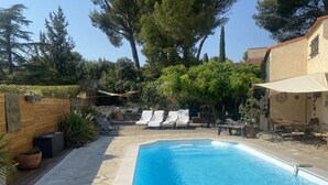 A swimming pool with lounge chairs and a table, surrounded by trees and a wooden fence. - VILLA PROVENÇALE with private pool (between Aix and Marseille) (VELAUX)
