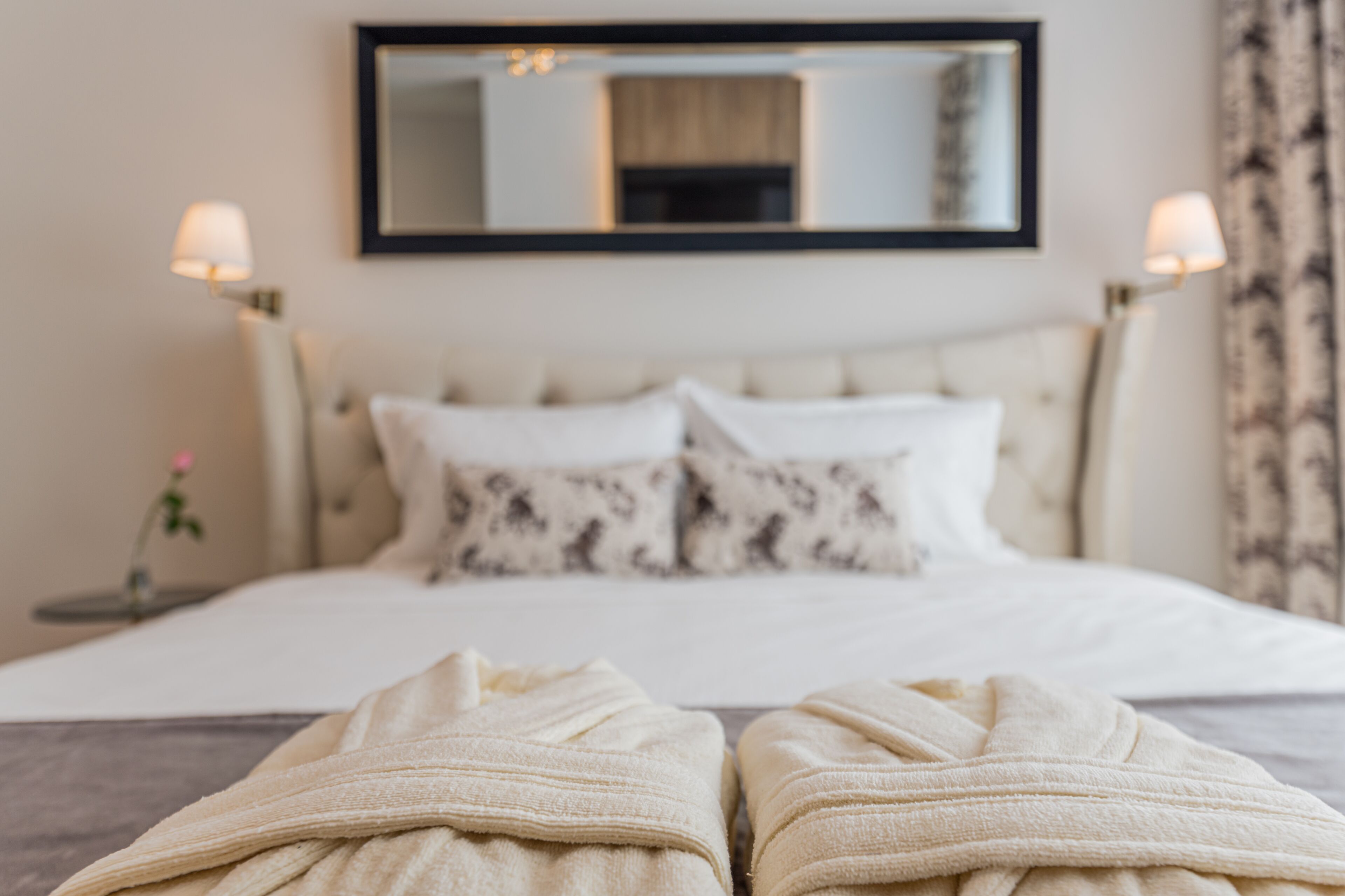 Una cama bien hecha con cabecera, dos lámparas de noche y un espejo sobre la cama.