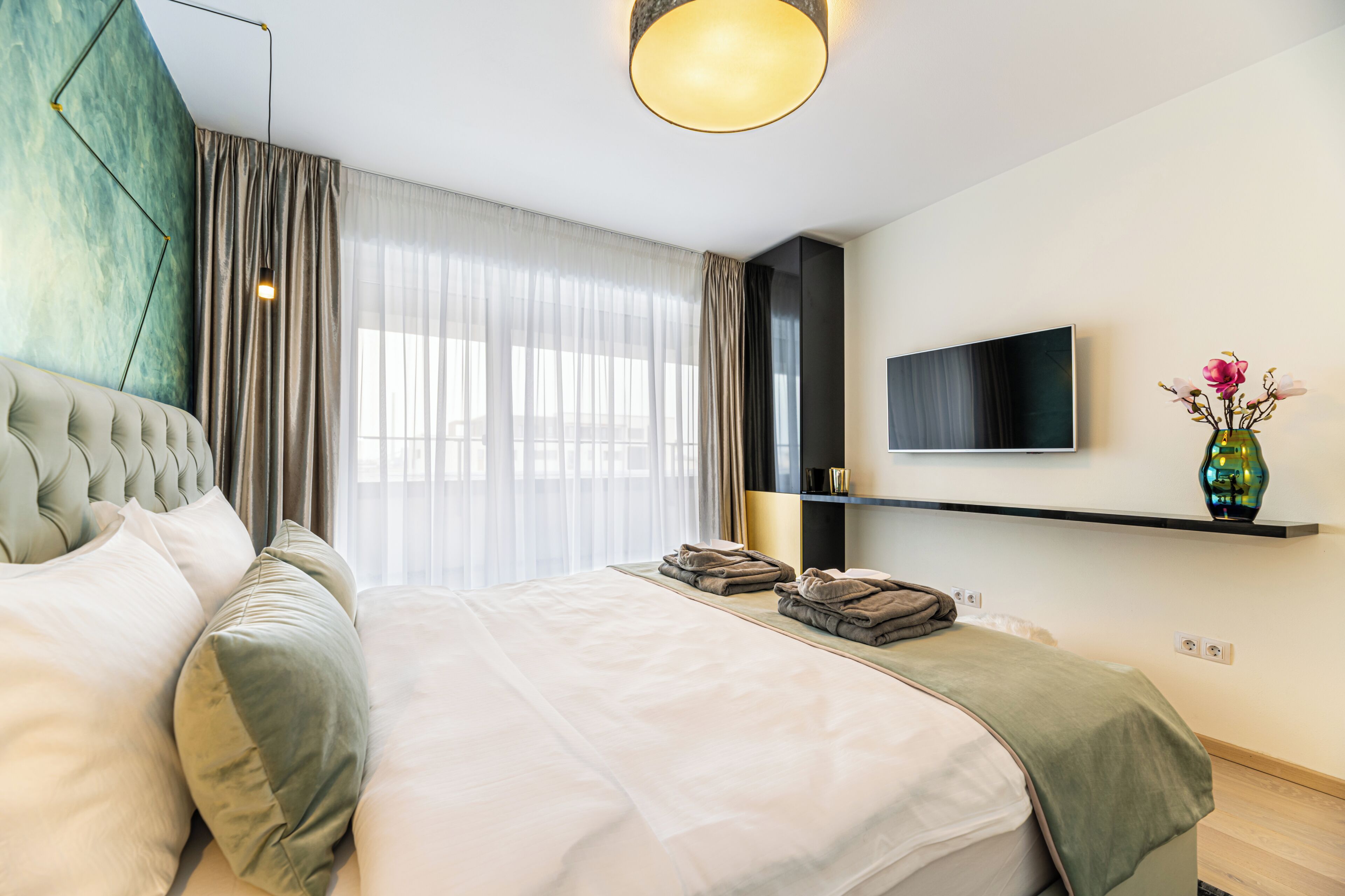 Une chambre d’hôtel avec un lit, un téléviseur fixé au mur et un vase rempli de fleurs posé sur une étagère.