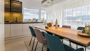 A modern kitchen with a wooden dining table, teal chairs, and a large window offering a city view. - MK Apartments Brasov (Brasov)