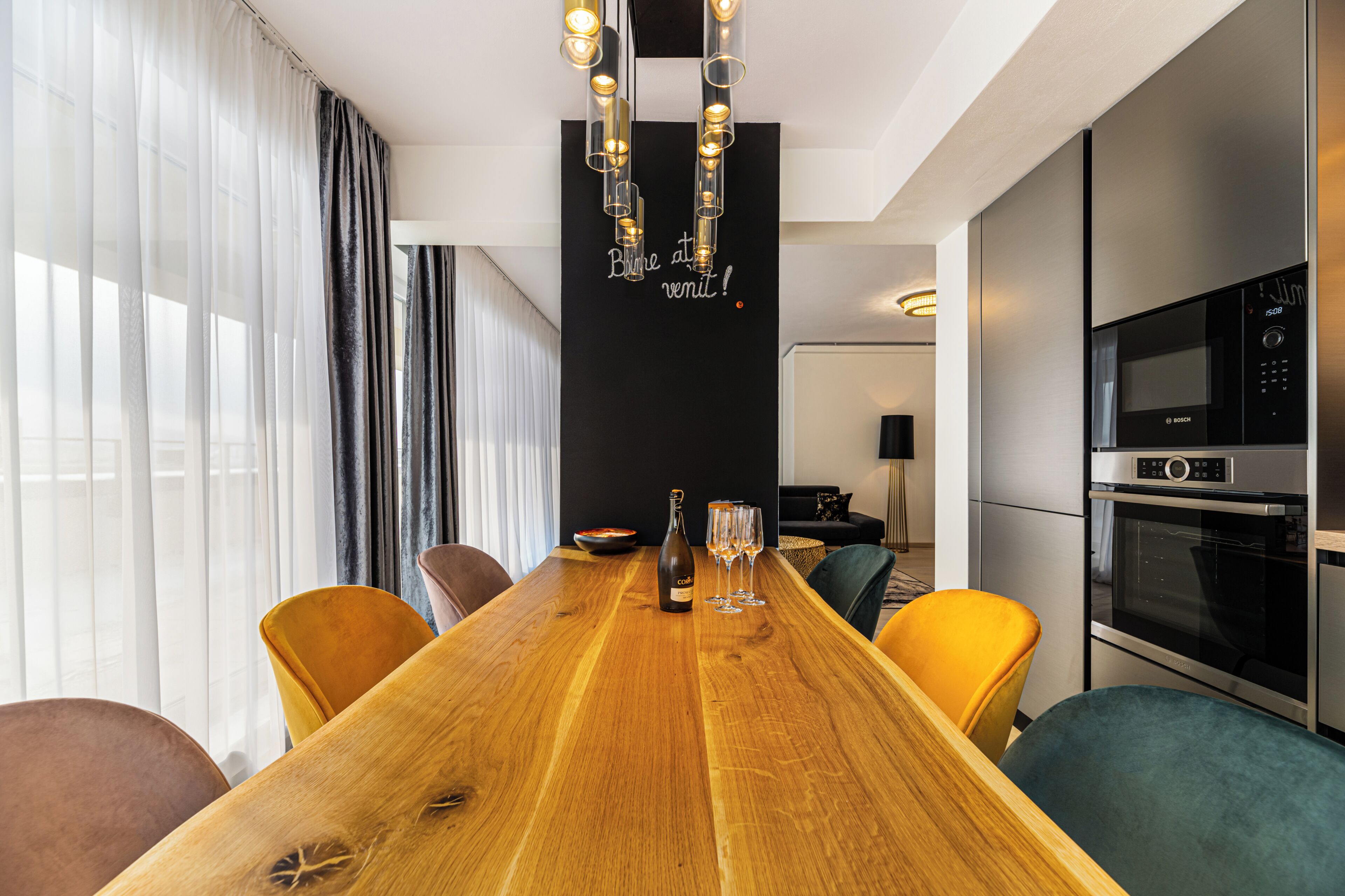 A modern kitchen with a Bosch oven and a dining area with a wooden table and yellow chairs.