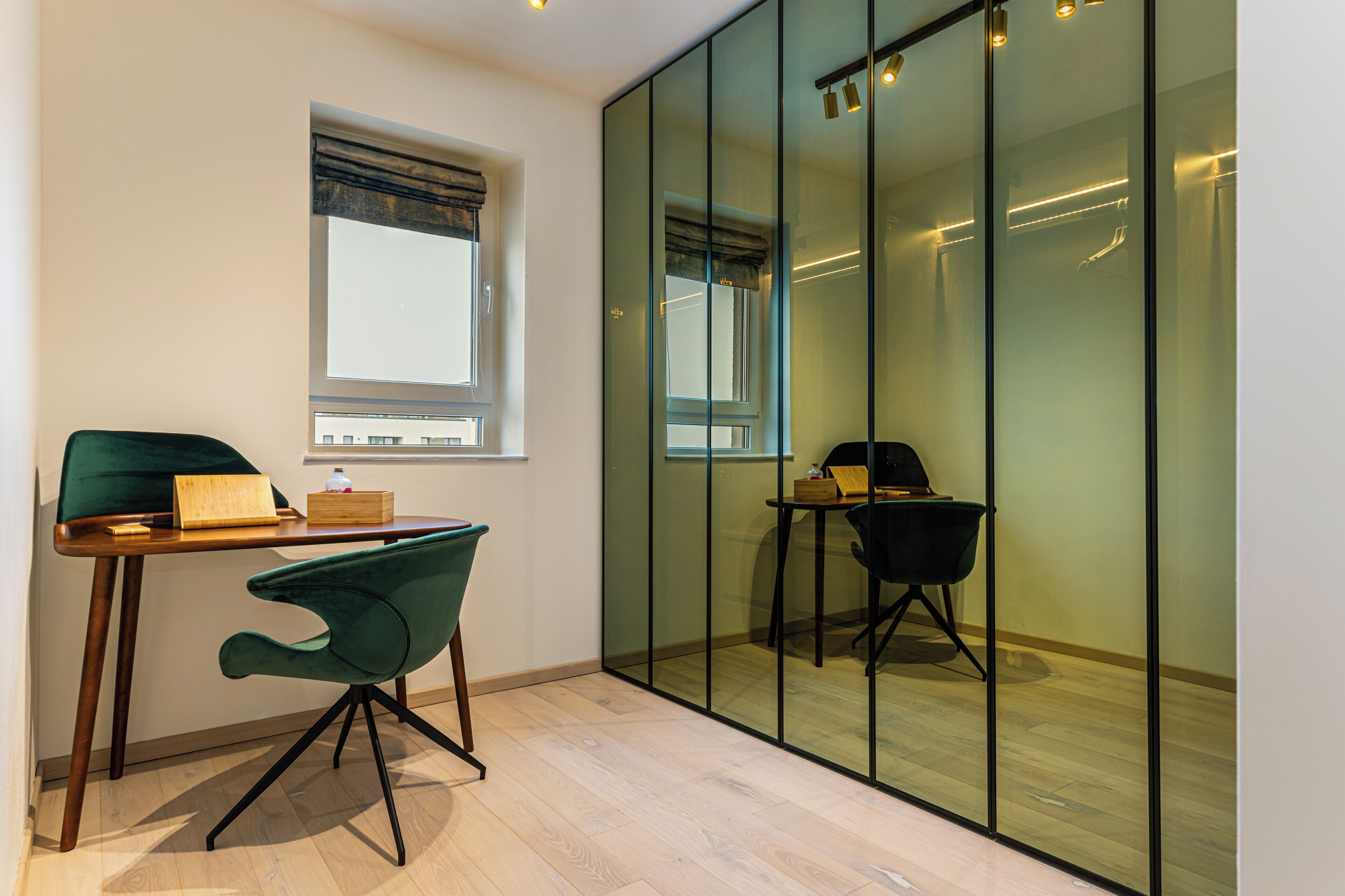 A modern room with a wooden desk, a green chair, a small table with a box, and a window with a view.