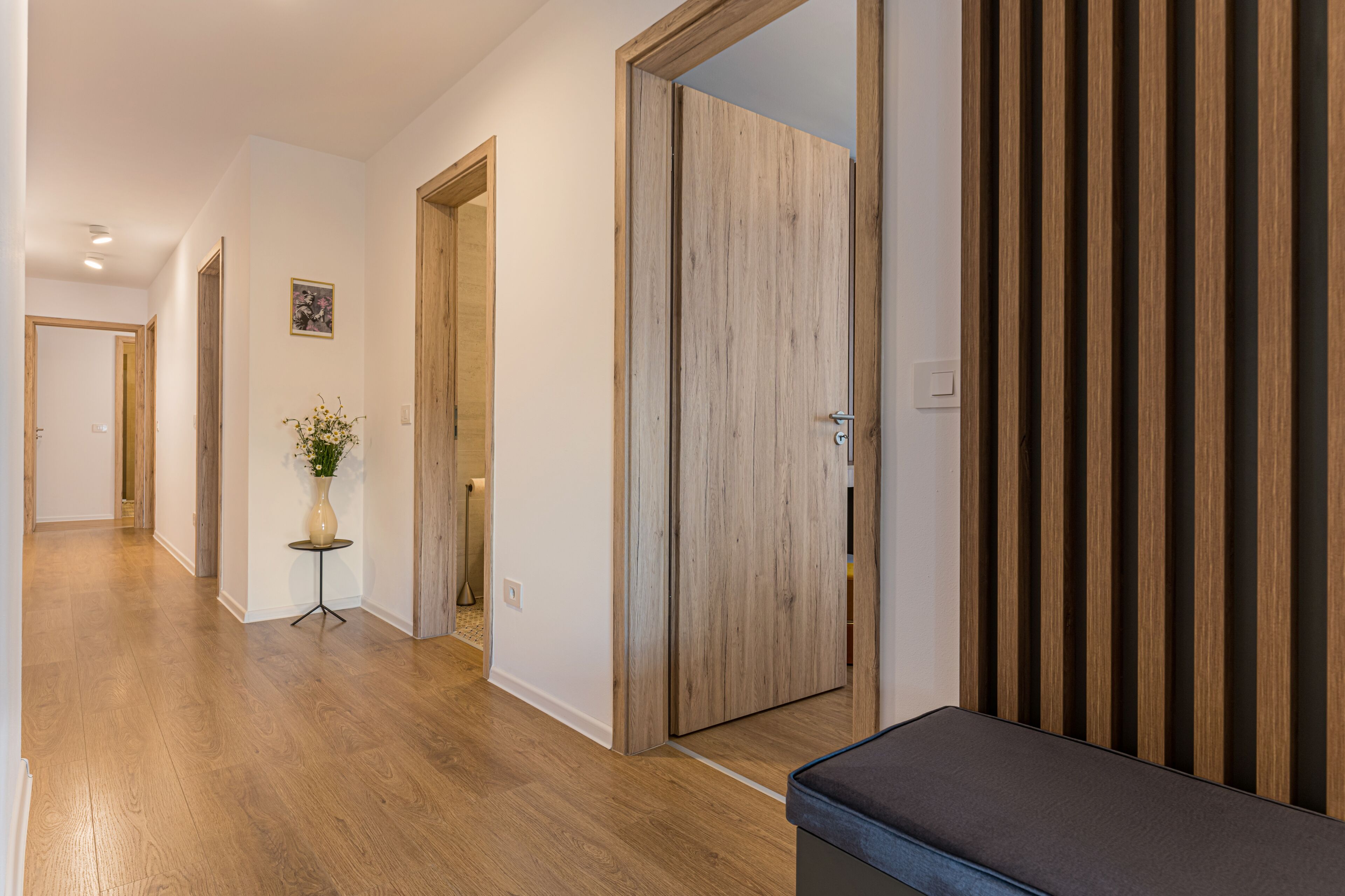 Un couloir doté d’un plancher en bois, d’un banc et d’une porte ornée de panneaux de bois verticaux.