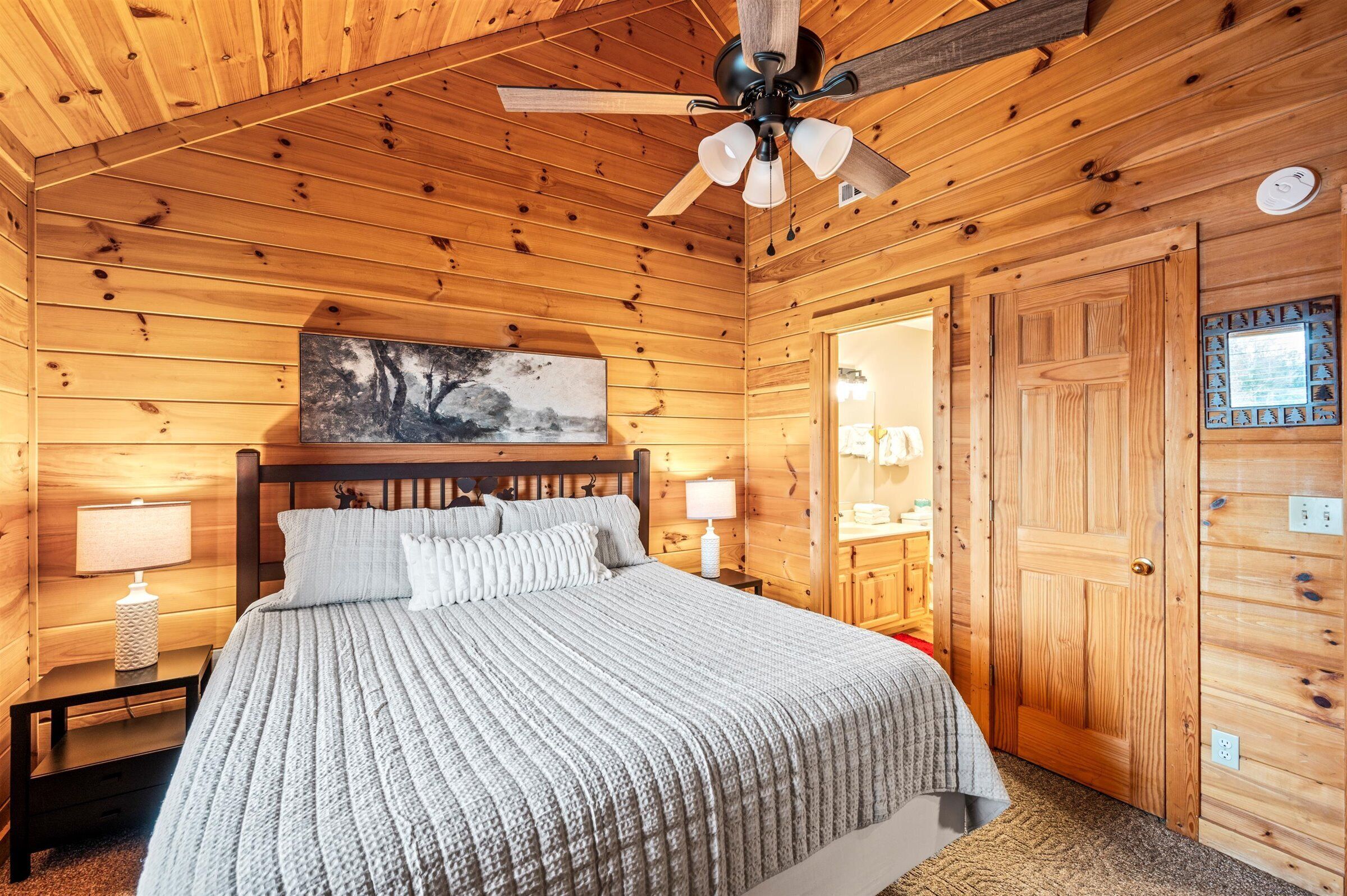 A wooden-paneled bedroom with a bed, nightstands, a ceiling fan, and a door.