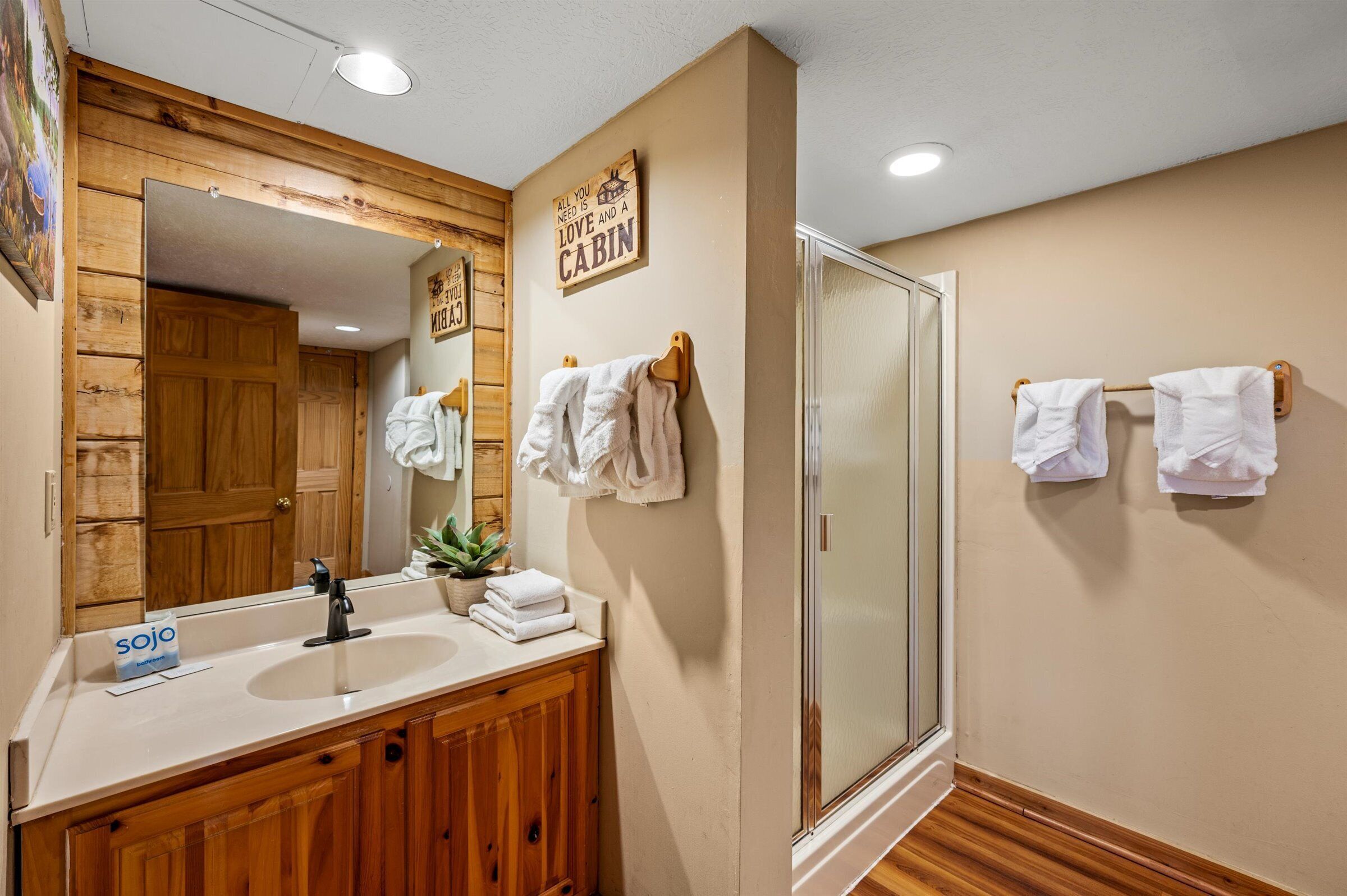 A bathroom with a wooden vanity, a sink, a mirror, a shower, and towels hanging on hooks.