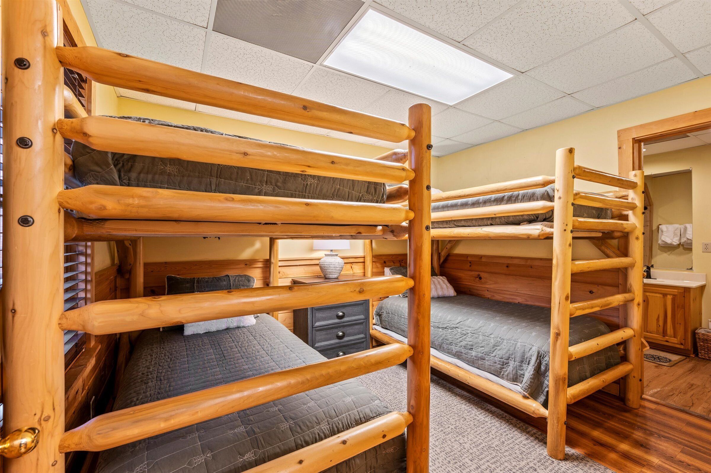 A bunk bed room with wooden railings, a small bedside table, and a lamp.