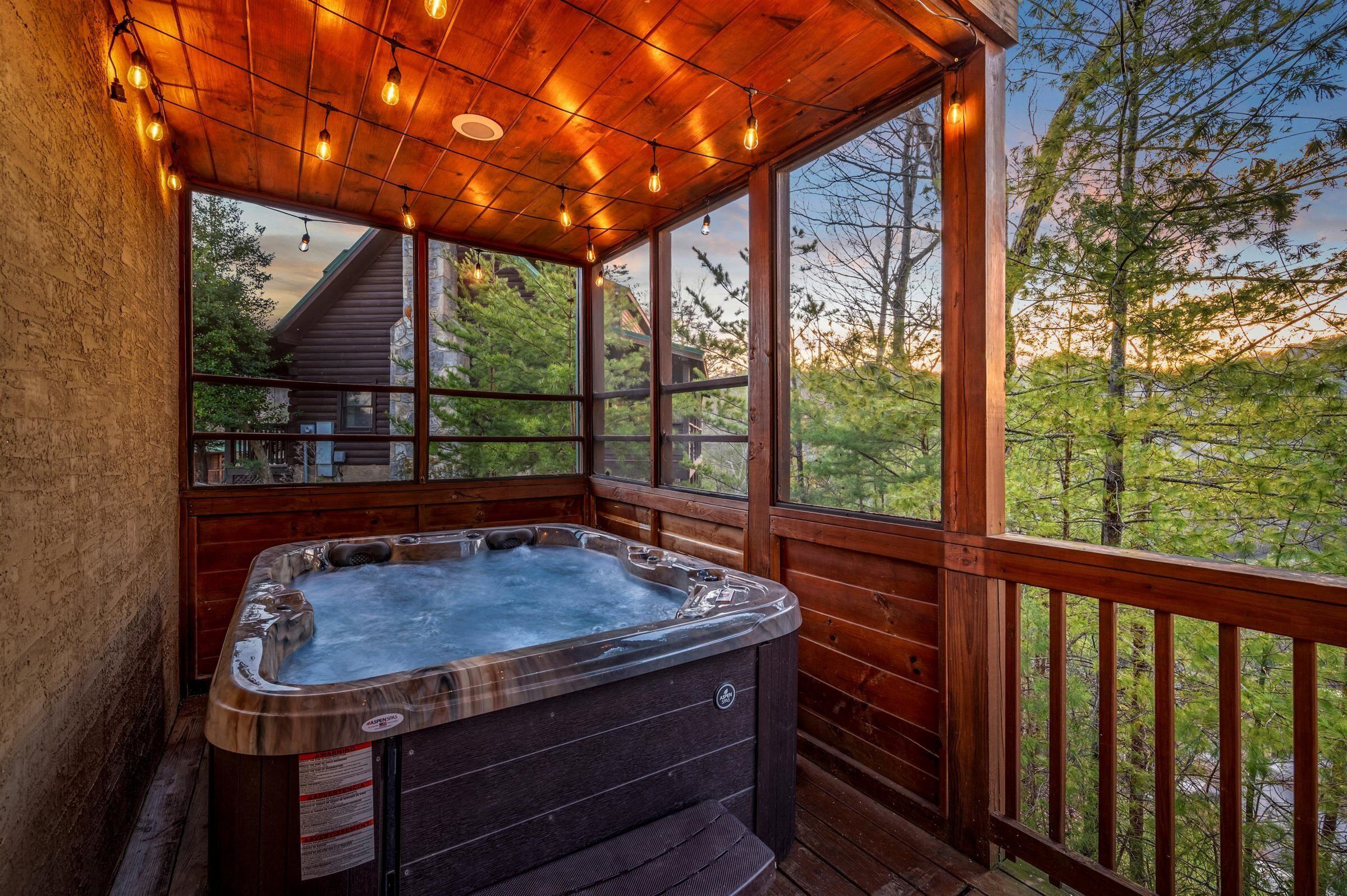 Una terraza de madera con un jacuzzi, ventanas grandes y una cabaña al fondo.